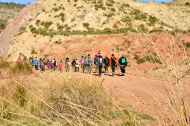 Grup kum ve taşların dağ inanılmaz bir manzara ile arka plan üzerinde yürüme muhteşem güneşli bir günde yola trekking renkli sırt çantası ile yetişkin insan