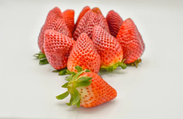 Vista dall'alto verso il basso di un gruppo di diverse fragole rosse fresche gustose appena raccolte e pronte per essere mangiate. Le fragole sono messe con le foglie verdi su fondo bianco tranne una. Foto orizzontale — Foto Stock