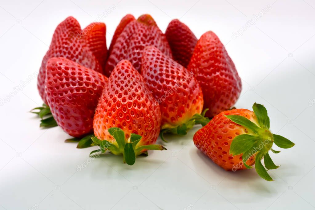 top down view of a group of several tasty fresh red strawberries just harvested and ready to be eaten. The strawberries are put with the green leaves on a white background but one. Horizontal photo
