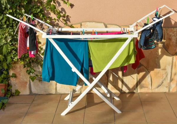 Camisas de colores, calcetines, pijamas, camisetas, calzoncillos, guantes y otra ropa mojada después de haber sido lavada, mantenga una línea de lavado al sol para secarse en la terraza de un jardín en un día soleado . — Foto de Stock