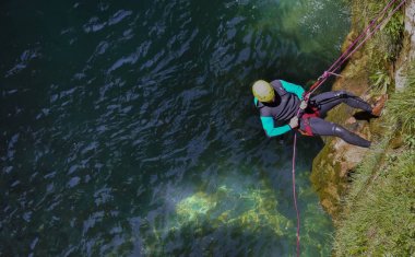 bir neneopren oturup sarı kask giyen bir adamın cenital görünümü yaz bir gün kanyon için nehir suyuna gitmek için kayalar ve bitkilerin dikey bir uçurum akayan dizeleri ile inen