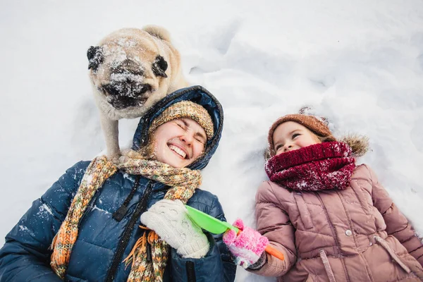 Mom and daughter are lying in the snow, talking with the dog, snow and games