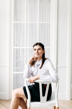Açık renk elbiseli bir kız, bir odada bir sandalyede oturuyor, iç mekan, model, portre, güzellik, gençlik, kendine bakım, danışmanlık, iş, müdür.