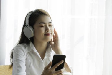 Güzel genç asyalı kadın akıllı telefon kullanımı ve kulaklık müzik dinleme.