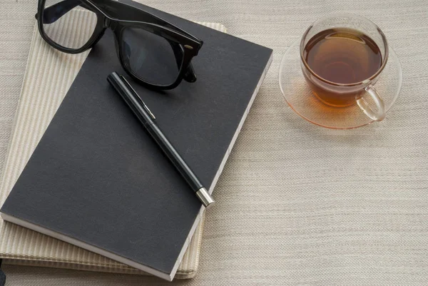 One glass pen, notebook, glasses and tea