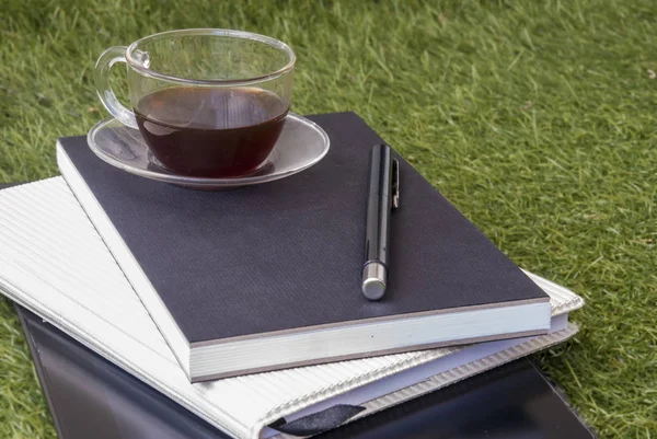 Einen Stift, ein Notizbuch, ein Tablet und ein Glas Tee auf dem Rasen — Stockfoto