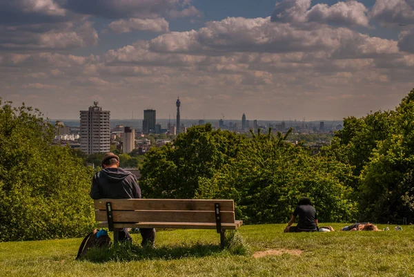 A men sit on a wooden chair at Hampstead Heath with a beautiful — Stock Photo, Image