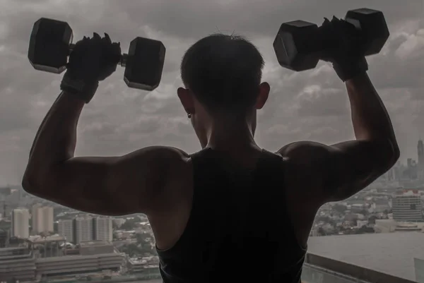 The back of Handsome man train muscles with a lifting weights du