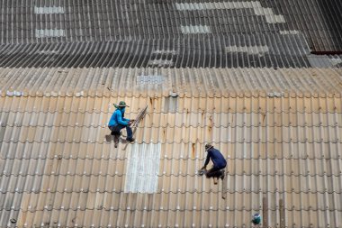 Bangkok, Tayland - 13 Haziran 2020: Hasarlı fabrikanın çatısındaki fayansları tamir eden iki işçi.
