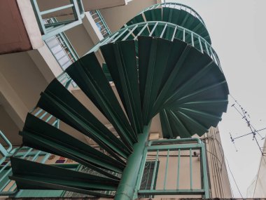 Aşağıdan yeşil spiral merdiven manzarası. Avlu mimarisinde spiral merdiven dairesi. Açık merdiven dekorasyonu iç mimarisi. Seçici odak.