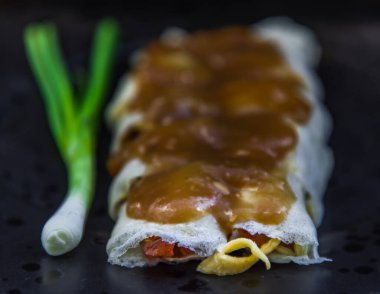 Taze Tayland böreklerinin yakın plan çekimi. Üstünde tatlı sos ve siyah tabakta taze soğan var. Seçici odak.