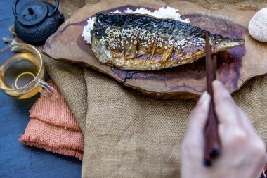 El, yemek çubuklarını kullanarak, Japon usulü sıcak çay ile servis edilen ahşap zemin üzerinde teriyaki soslu pilav ızgara balık topluyor..