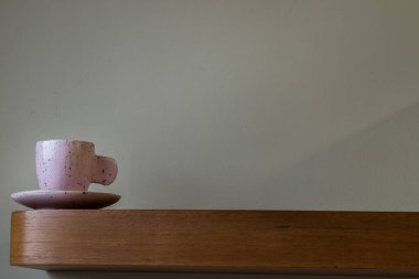 Oturma odasının duvarındaki ahşap rafta el yapımı pembe seramik bardak. Ev dekoru. Mesaj için yer var. Seçici odak.