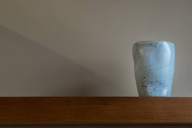 Oturma odasının duvarındaki ahşap rafta el yapımı mavi seramik bardak. Ev dekoru. Mesaj için yer var. Seçici odak.