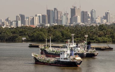 Bangkok, Tayland - 04 Ocak 2020: Nehrin ortasına ve Chao Phraya Nehri kıyısındaki yeşil bir ağacın önüne park edilmiş iki kargo gemisi.