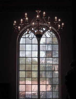 Royal Tunbridge Wells, İngiltere - 29 Nisan 2025 - Tavandan sarkan güzel bir Chandelier manzarası ve Kral Şehit Charles Kilisesi 'nin arka planında kemerli cam pencereler. Duvar kağıdı, poster ve boşluk olarak kullan.