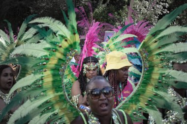 Sanatçı, Notting Hill Karnavalı 'nın büyük tüylü başlığı ve süslü mücevherleriyle süslü renkli ve çetrefilli bir kostüm giyerek Karayip kültürü ve tarihi kutlamalarıyla tanınıyor.