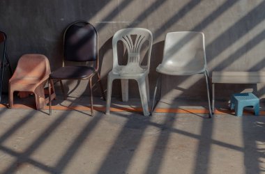 Bangkok, Tayland 05 Ocak 2025 - Sabah güneşiyle farklı sandalyeler manzarası tahta bataryaların önünde apartman binasının içindeki eski beton duvarın önünde parlıyor. Metin için duvar kağıdı, poster ve boşluk olarak kullan.