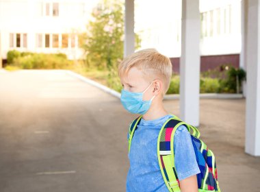 Okula dönelim. Kızın yüzünde okul çantasıyla koruyucu bir maske takmış okul çağındaki bir çocuk. 2020 'de yeni okul yılı. Kişisel koruma ekipmanları.
