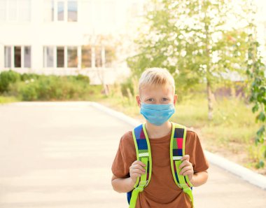 Okula dönelim. Kızın yüzünde okul çantasıyla koruyucu bir maske takmış okul çağındaki bir çocuk. 20.C 'de yeni okul yılı. Kişisel koruma ekipmanları.