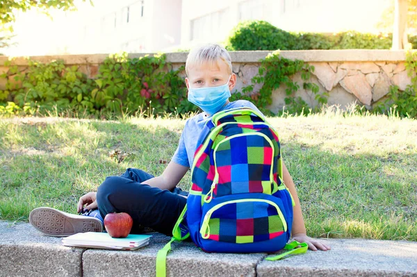 学校を背景にした幸せな笑顔の学童 健康保護のために医療面マスクを身に着けている学校の少年 学校に戻る 学びの概念 — ストック写真