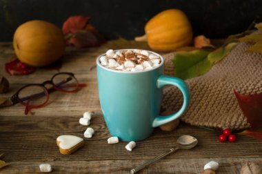 Sonbahar yaprakları ve ahşap bir masanın üzerinde balkabakları olan mavi seramik bir kupada kremalı sıcak kakao. Hygge konsepti, samimi sonbahar, Şükran Günü, sonbahar. Sıcak içecekler. Sakin bir sonbahar hayatı..