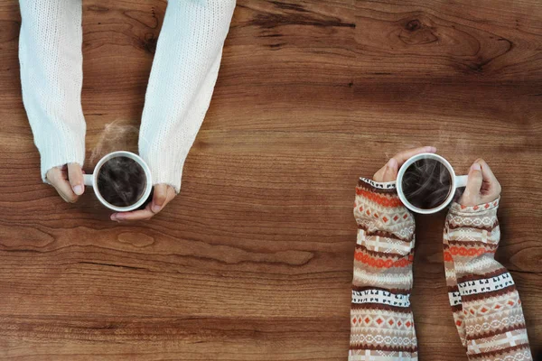 Female hands holding cups of coffee on rustic wooden table background — Stock Photo, Image