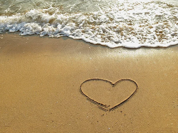 Heart drawn on the sand of a sea beach with white wave at sunset time Stock Photo