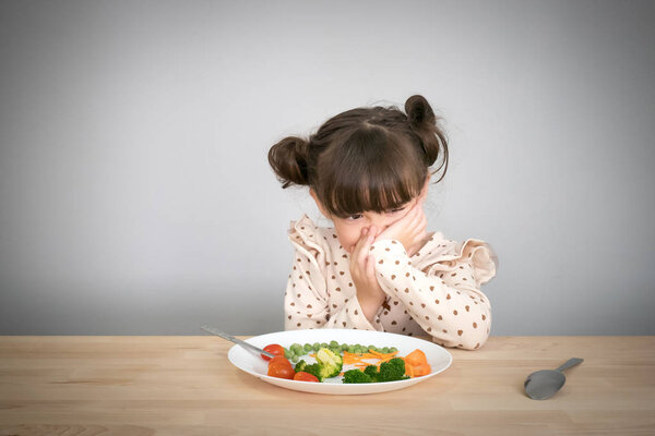 Nutrition & healthy eating habits for kids concept. Children do not like to eat vegetables. Little cute kid half race girl refuse to eat healthy vegetables.