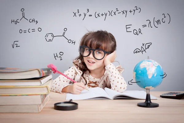 Concetto di istruzione. carina bambina a scuola felice di fare i compiti. equazioni matematiche e formula chimica in background — Foto Stock