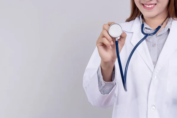 Młoda azjatycka lekarka trzymająca stetoskop z uśmiechniętą twarzą na szarym tle. koncepcja opieki zdrowotnej — Zdjęcie stockowe