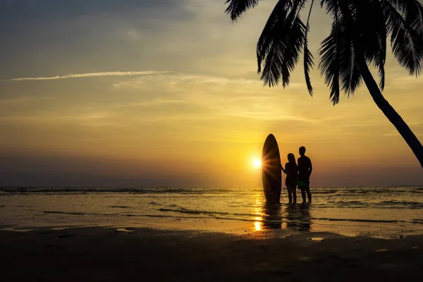 Man en meisje met surfplank op het strand bij zonsondergang — Stockfoto