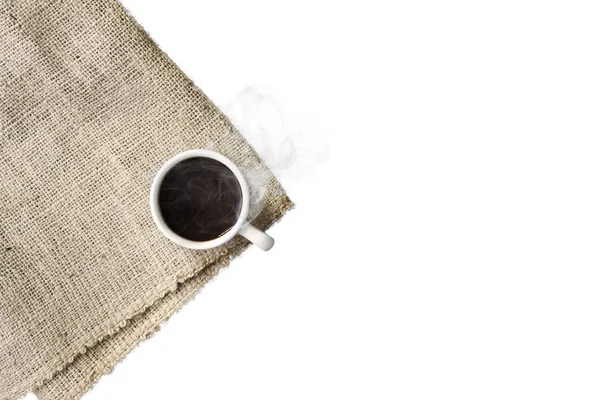 A cup of black coffee with smoke on sackcloth napkin, isolated on white background. — Stock Photo, Image