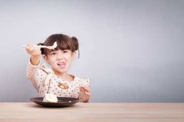 Çocuklar yeme konsepti zevk : Mutlu küçük sevimli karışık yarış kız gülen yüz ile pasta yeme zevk , dil sopa elinde kaşıkla yemek için davet. Çocuk poster arka plan.