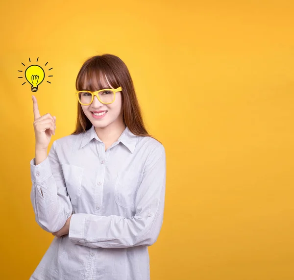 Business Asian woman with yellow vintage glasses stand and have idea lamp bulb light on fingertip, yellow background with copy space for design for poster and advertising text. Asia model in her 20s. — Stock Photo, Image