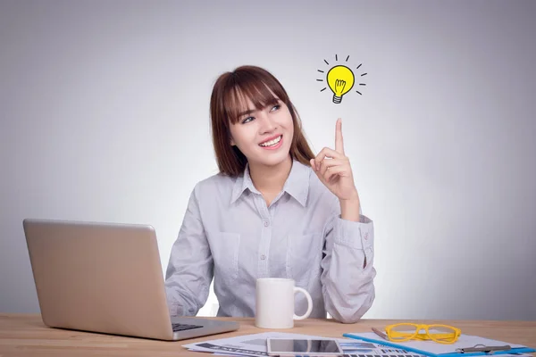 Success growing business concept : Thinking business woman looking up with light idea bulb above finger isolated on gray wall background. Portrait of young Asian model in her 20s — Stock Photo, Image