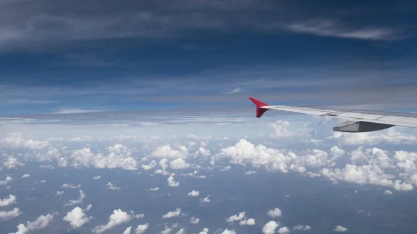 Concepto de viaje en avión: Vista desde la ventana del avión. Nubes y cielo azul bajo el ala del avión como se ve a través de la ventana de un avión en gran ángel con espacio de copia para el fondo de la agencia de viajes — Foto de Stock