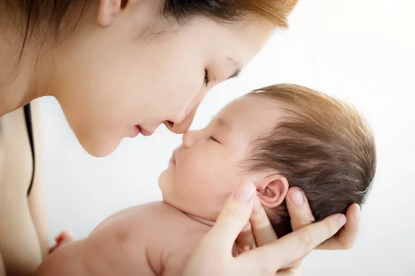 Concepto de amor y relación familiar: Retrato de la madre asiática feliz usar la nariz toque recién nacido linda nariz bebé en una cama blanca en casa. Padre e hijo pequeño abrazo relajante y beso en casa . — Foto de Stock