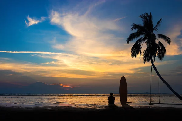 Silhouet van Surf man zitten met een surfplank op het strand. Surf scène bij Sunset Beach met kleurrijke hemel. Outdoor water sport avontuur levensstijl. Zomeractiviteit. Knappe Asia mannelijk model in zijn 20s. — Stockfoto