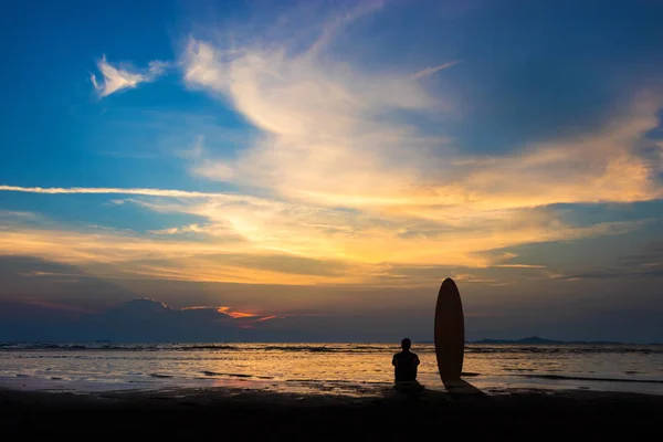 Silhouet van Surf man zitten met een surfplank op het strand. Surf scène bij Sunset Beach met kleurrijke hemel. Outdoor water sport avontuur levensstijl. Zomeractiviteit. Knappe Asia mannelijk model in zijn 20s. — Stockfoto