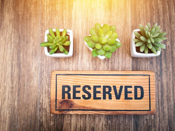 Wooden reserved sign on top of a wooden table in a restaurant, Reservation seat at restaurant for dating on celebrate day concept. Reserved sign from top view decorate with little cactus and light