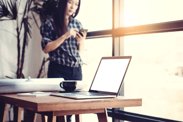 İşyeri konseptinde teknoloji. Modern ofiste genç Asyalı iş kadını iş için telefon kullanarak. Boş beyaz ekran dizüstü bilgisayar ve plan masada. — Stok fotoğraf