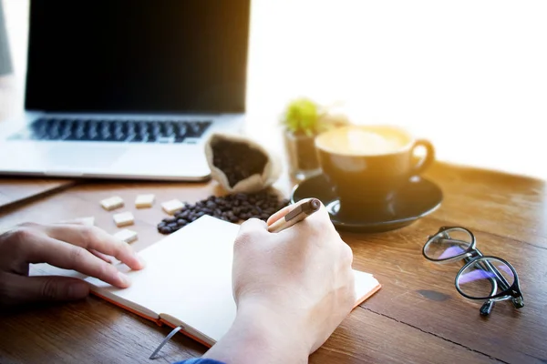 Férfi menedzser üzembe ötleteit és az írás üzleti terv a munkahelyen, az ember kezében tollat és tudomásul véve a notebook, az asztal az irodában, szüreti színes, reggeli fény, szelektív fókusz. — Stock Fotó