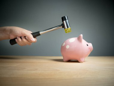 Piggy bank, savings, investments ,currency concept : A hand holding a hammer which is raised above a pink sad piggy bank, with a shocked and apprehensive facial expression. clipart
