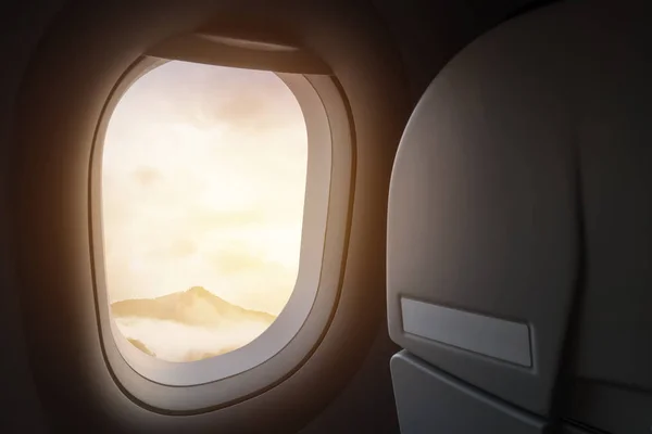 Viaje y viaje en avión concepto. vista de la hermosa montaña y la niebla con luz solar dorada y destello de lente como se ve a través de la ventana de un avión —  Fotos de Stock