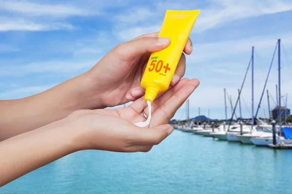 woman applying sunscreen on her hand with blur boats docked at the yacht club background. SPF sunblock protection concept. Travel vacation
