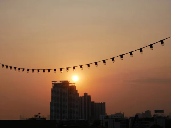 Bangkok vista della città dal tetto edificio al tramonto prima del tramonto con lampadina filo elettrico appeso in primo piano. immagine del tramonto in città per sfondo carta da parati . — Foto Stock