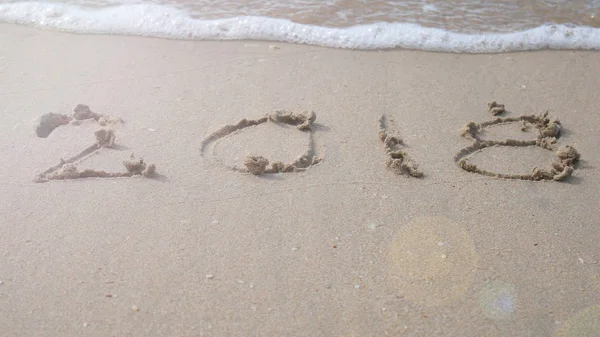 happy new year 2018.  2018 write on sandy beach with wave splash. countdown for happy new year turning from year 2017 to 2018 background