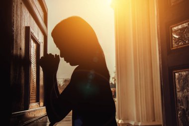 silhouette of woman kneeling and praying in modern church at sunset time clipart