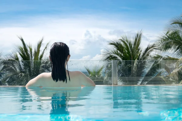 sexy woman in bikini swimming suit relaxing in the luxury private swimming pool on the beach with palm tree at sea side. holiday and vacation on the tropical beach at summer season concept